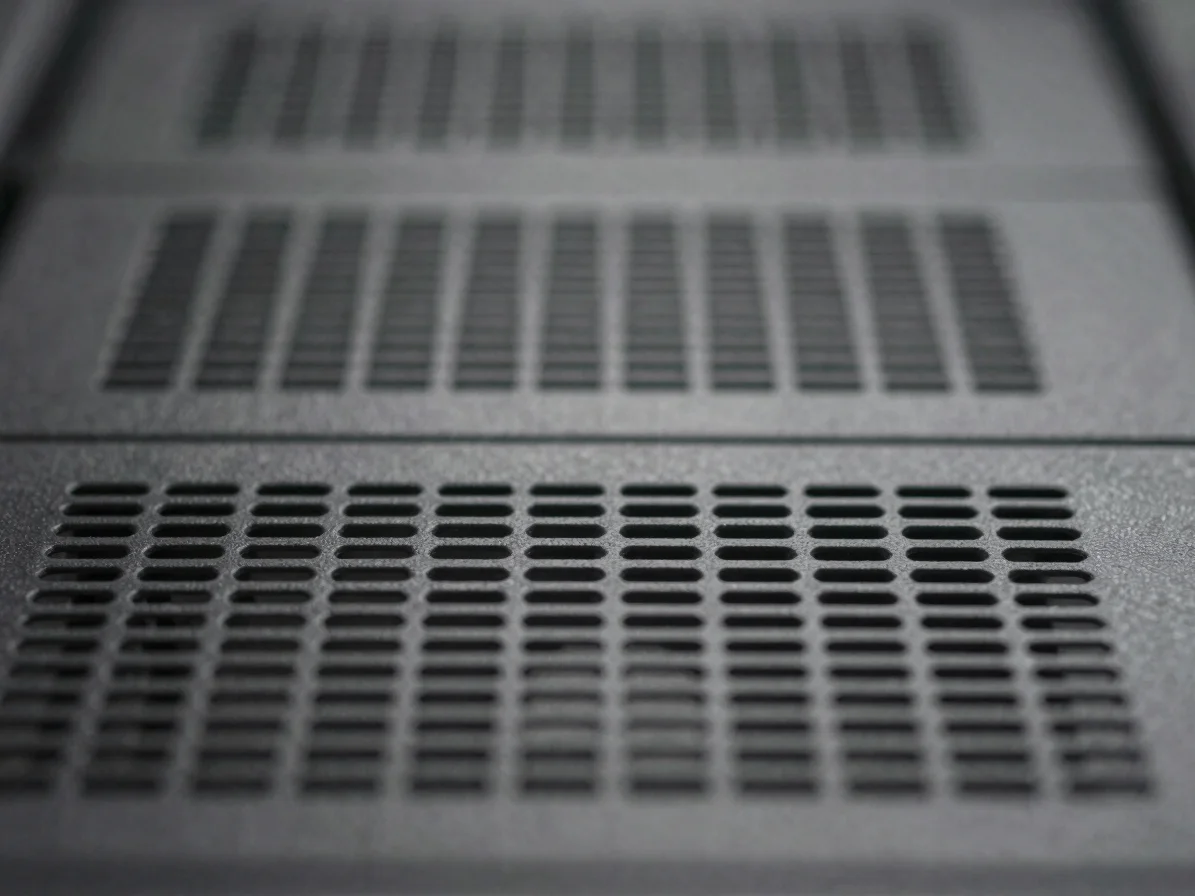 Macro detail of a server rack's ventilation grilles, muted slate charcoal tones, soft diffused light, abstract compositi